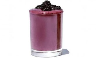 A glass filled with a acai berry combo smoothies, purple smoothie topped with plump blackberries on a white background.