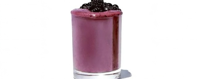 A glass filled with a acai berry combo smoothies, purple smoothie topped with plump blackberries on a white background.